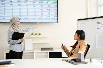 Confident  business professional woman wearing hijab talking to female colleague at office table, speaking, gesturing, teaching, explaining work tasks.