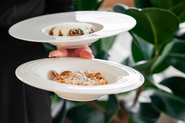 Two white plates with delicious food, one covered in melted cheese, the other with pasta and grated...