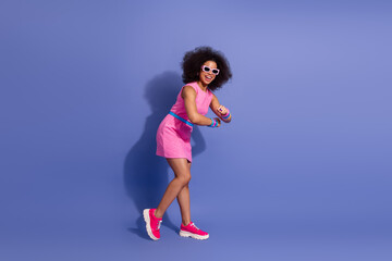Fashionable young woman with vibrant style posing against a purple background, wearing a pink...