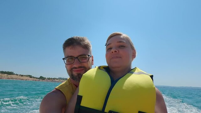 Happy family shoot yourself on action camera while riding banana boat on blue sea on summer day. Water attraction. Travel holiday vacation