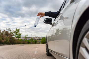 Man hand throwing a used water bottle from his car window onto the road.