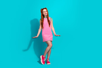 Young stylish girl with red hair in a checkered dress posing playfully against a vibrant turquoise background