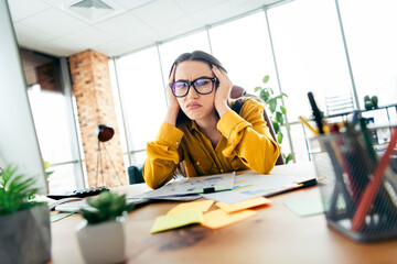 Young businesswoman frustrated at her workstation in a modern office space, struggling with tasks...