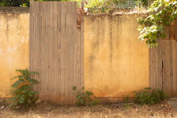 Fototapeta premium Stock photo of an old wooden fence beside a weathered yellow stucco wall. Perfect for rustic, vintage, or architectural designs.