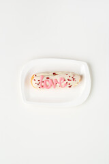 Delicate pastry topped with pink icing and heart sprinkles on a white plate
