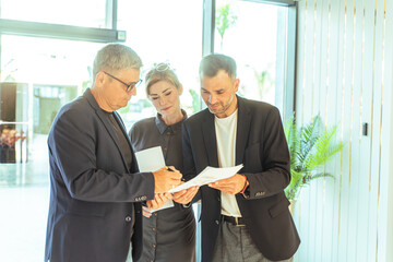A group of business professionals reviews documents in a modern office, advises lawyers, and...