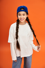 Stylish teenage girl poses confidently in trendy outfit against an orange backdrop