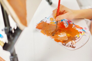 Fototapeta premium Close-up of a little girl hand mixing paint with a brush on a palette