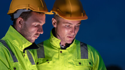caucasian white engineers in safety uniforms and helmets using laptop and radio for site...