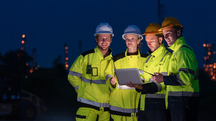 caucasian white engineers in safety uniforms and helmets using laptop and radio for site communication. Concept of teamwork, inspection, and operations at an industrial facility.Construction of Oil, 