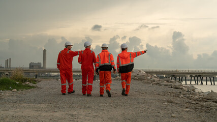 caucasian white engineers in safety uniforms and helmets using laptop and radio for site communication. Concept of teamwork, inspection, and operations at an industrial facility.Construction of Oil, 