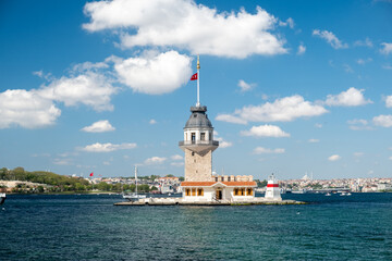 Fototapeta premium Historic Maiden's Tower in Istanbul with sightseeing boats docking on a sunny day, featuring Bosphorus waters, blue sky, city skyline, and iconic Turkish architecture.