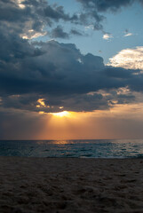 Soft golden light illuminates an empty sandy beach and the calm Black Sea in Odesa Ukraine after a storm has passed, with lingering dark clouds creating a serene and hopeful dawn scene.