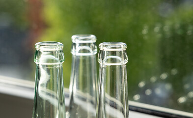 Bottle neck of white glass bottles infront of the window. Trees and sky in the background.