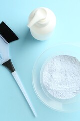 Bleaching powder and hairdresser's tools on light blue background, flat lay