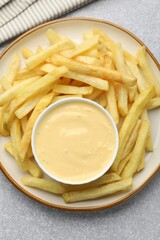 Tasty cheese sauce in bowl and French fries on grey table, top view