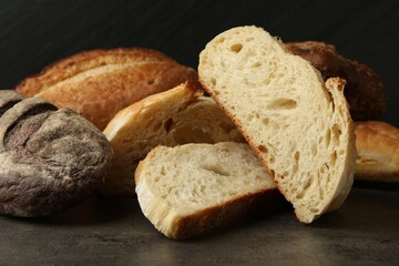 Different types of fresh bread on dark textured table against black background, closeup