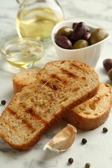 Toasted bread with oil, olives and spices on white marble table, closeup