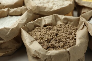 Different types of flour in paper bags on white table, closeup