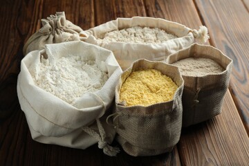 Different types of flour in bags on wooden table, closeup
