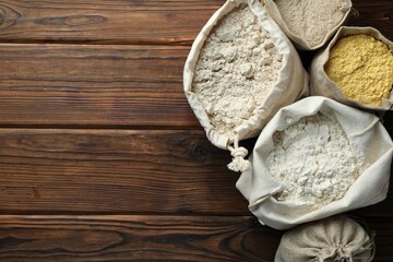 Different types of flour in bags on wooden table, flat lay. Space for text