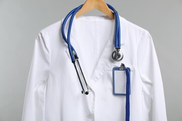 Doctor's coat with stethoscope and badge on hanger against grey background