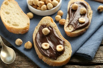 Slices of bread with chocolate spread and hazelnuts on wooden table, closeup
