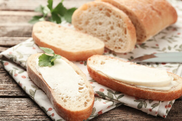 Pieces of bread with butter and parsley on wooden table, closeup