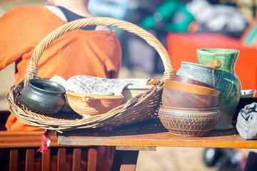 Assortment of rustic handmade bowls, cups, and jugs in a wicker basket on display at traditional outdoor market stall. High quality photo