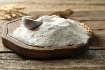 Wheat flour, spikelets and spoon on wooden table, closeup