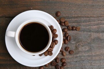 Aromatic coffee in cup, beans and saucer on wooden table, flat lay
