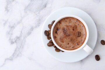 Aromatic coffee in cup, beans and saucer on white marble table, top view. Space for text