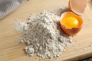 Pile of flour and broken egg on wooden board, closeup