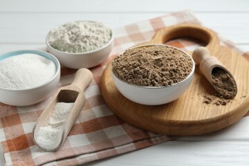 Different types of flour in bowls and scoops on white wooden table, closeup