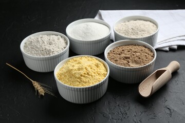 Different types of flour in bowls, scoop and spike on black textured table