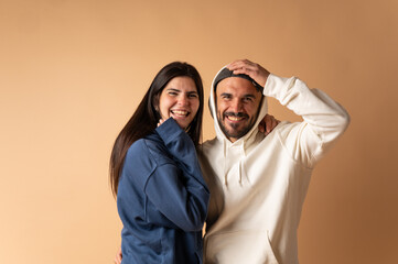 Happy couple laughing and embracing, wearing hoodies, on beige background
