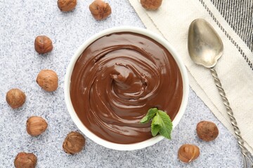 Tasty chocolate spread with mint in bowl and hazelnuts on grey textured table, flat lay