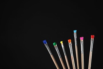 Many brushes with color paints on black background, closeup. Space for text