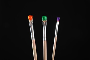 Three brushes with color paints on black background, closeup