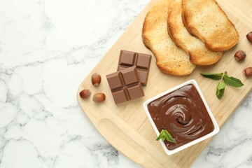 Tasty chocolate spread, pieces, toasts, mint and hazelnuts on white marble table, top view. Space for text