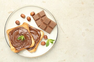 Toasts with tasty chocolate spread, pieces, mint and hazelnuts on light table, top view. Space for...