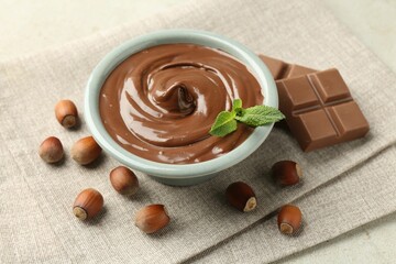 Tasty chocolate spread, pieces, mint and hazelnuts on light table, closeup