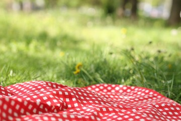 Red checkered blanket for picnic on green grass outdoors, closeup