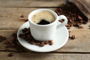 Aromatic coffee in cup and beans on wooden table, closeup