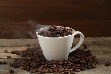 Aromatic coffee beans and cup on wooden table, closeup