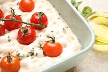 Raw focaccia with tomatoes and spices on light table, closeup
