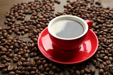 Aromatic coffee in cup and beans on wooden table, closeup