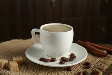 Aromatic coffee in cup, beans, brown sugar and cinnamon on table, closeup