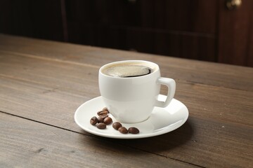 Aromatic coffee in cup and beans on wooden table, closeup