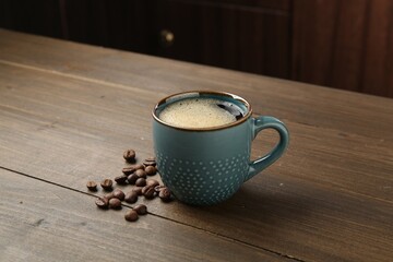 Aromatic coffee in cup and beans on wooden table